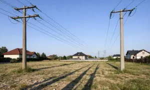 Likwidacja napowietrznej linii energetycznej. Dwa betonowe słupy z przewodami na tle domów i błękitnego nieba.