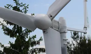Montaż elektrowni wiatrowej w pobliżu drzew. Białe łopaty wirnika i gondola na tle błękitnego nieba.