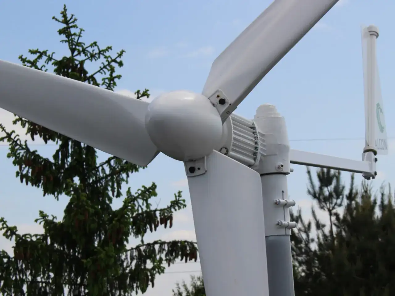 Montaż elektrowni wiatrowej w pobliżu drzew. Białe łopaty wirnika i gondola na tle błękitnego nieba.