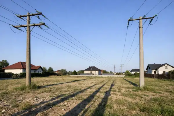 Likwidacja napowietrznej linii energetycznej. Dwa betonowe słupy z przewodami na tle domów i błękitnego nieba.