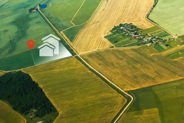 Działka rolna z warunkami zabudowy może stać się działką budowlaną. Widok z lotu ptaka na pola i wyznaczoną działkę z ikoną domu.
